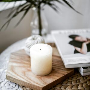A calming still life with a candle, magazine, and plant on a textured surface indoors.
